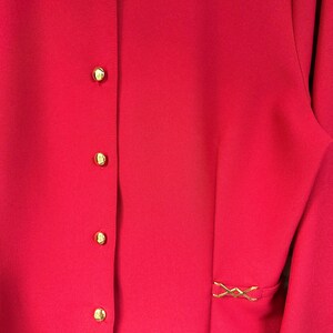 Puede incluir: Una chaqueta roja con cierre de botones dorados y un detalle decorativo dorado en la costura lateral.