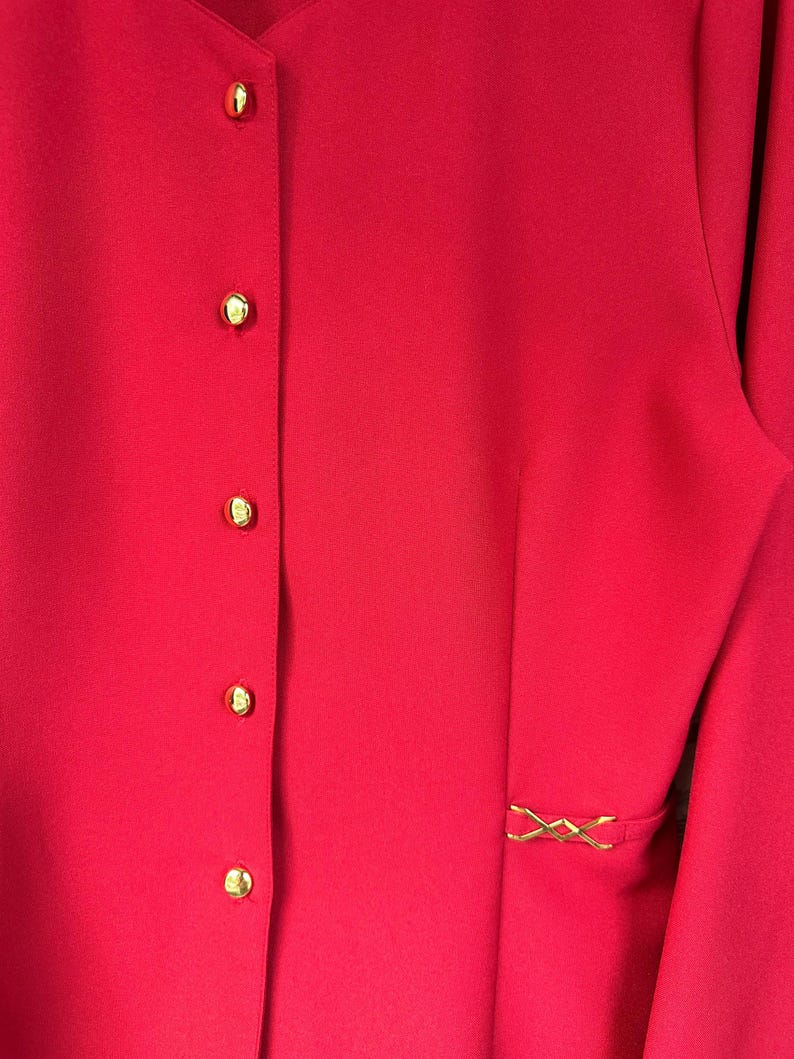 Puede incluir: Una chaqueta roja con cierre de botones dorados y un detalle decorativo dorado en la costura lateral.