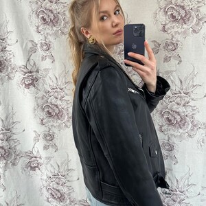 May include: A black leather motorcycle jacket with a zipper closure and a belt at the waist. The jacket has a stand-up collar and two pockets on the front.