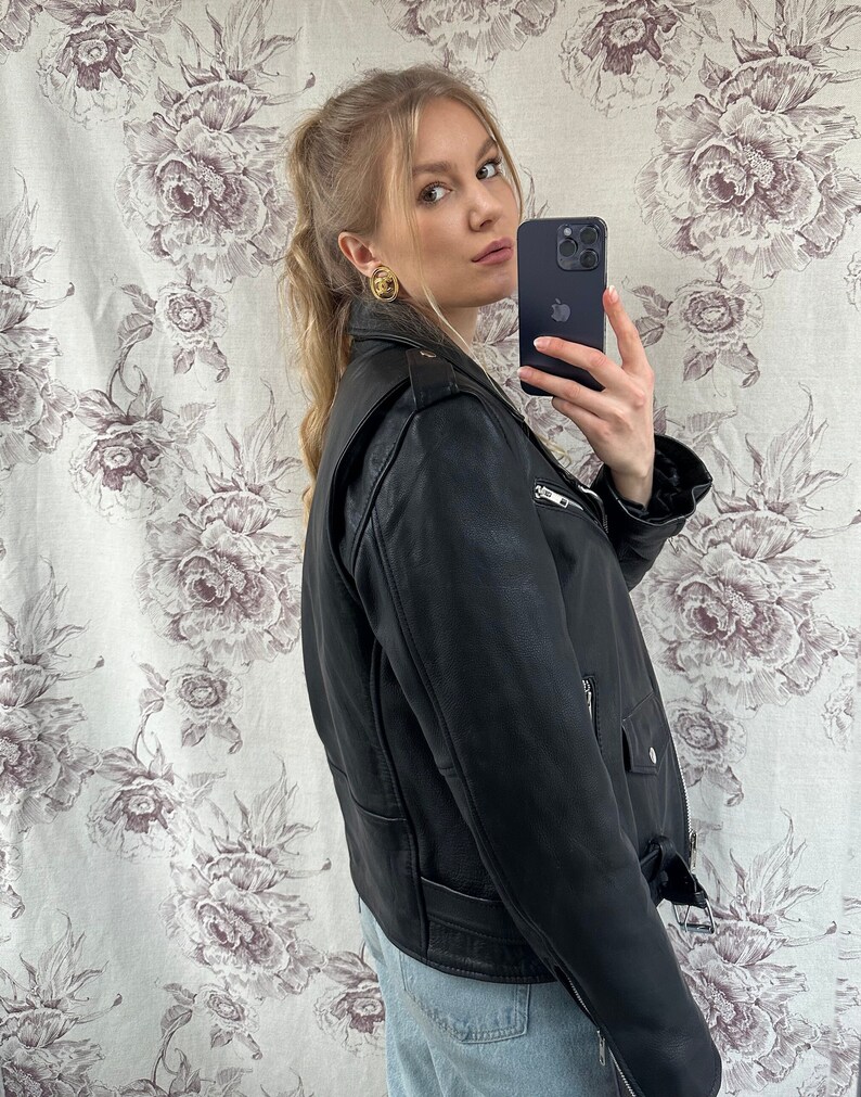 May include: A black leather motorcycle jacket with a zipper closure and a belt at the waist. The jacket has a stand-up collar and two pockets on the front.