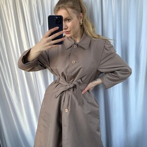 May include: A brown trench coat with a belt, button closure, and a collared neckline.