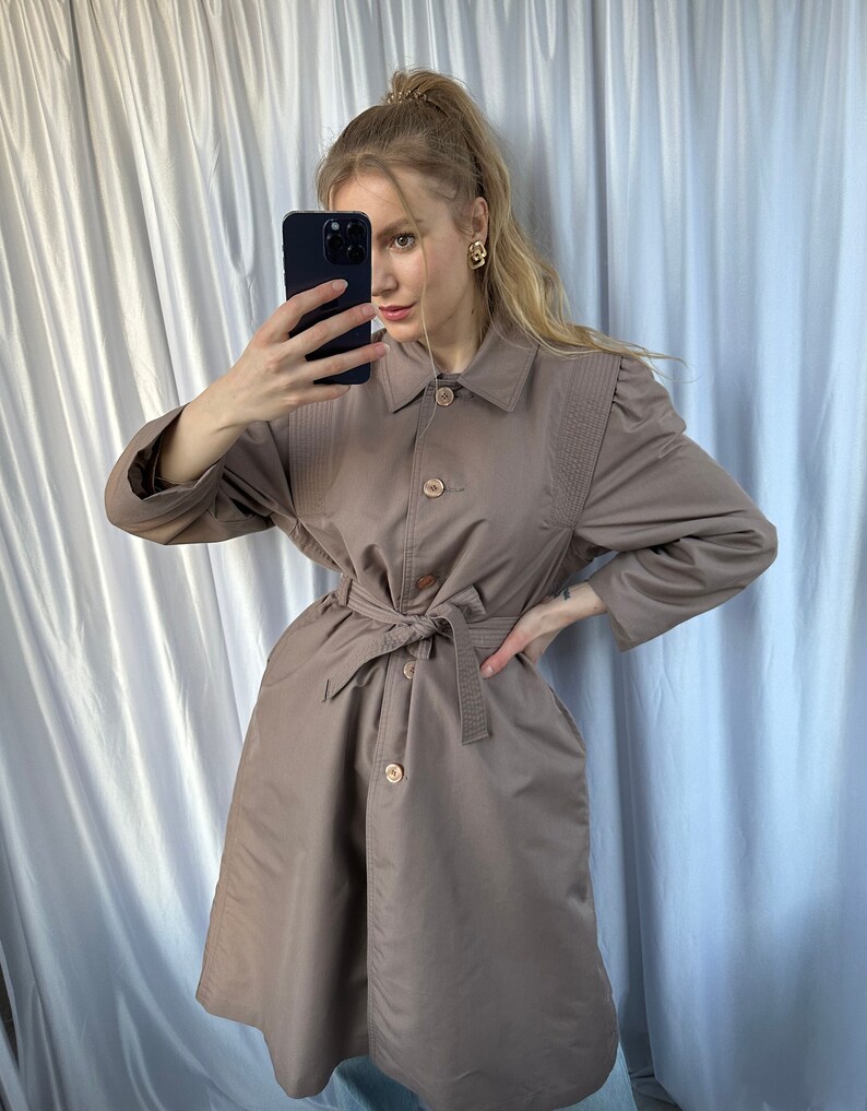 May include: A brown trench coat with a belt, button closure, and a collared neckline.