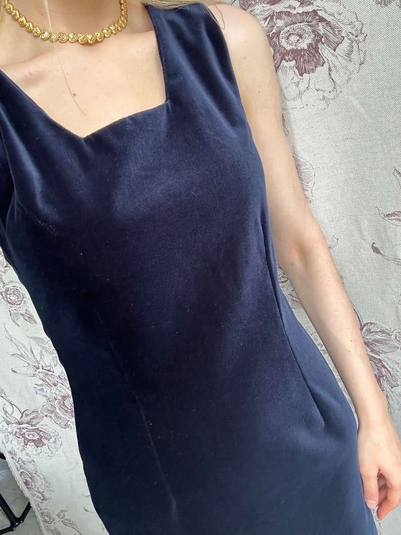 Pu&ograve; includere: Un abito senza maniche in velluto blu scuro con scollo quadrato.