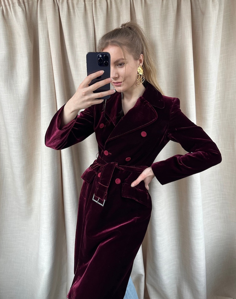 May include: A long, burgundy velvet coat with a double-breasted closure, a belt, and two front pockets.