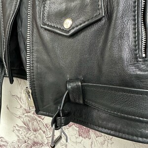 May include: Black leather jacket with a zipper closure, a large flap pocket on the front, and a belt with a metal buckle.