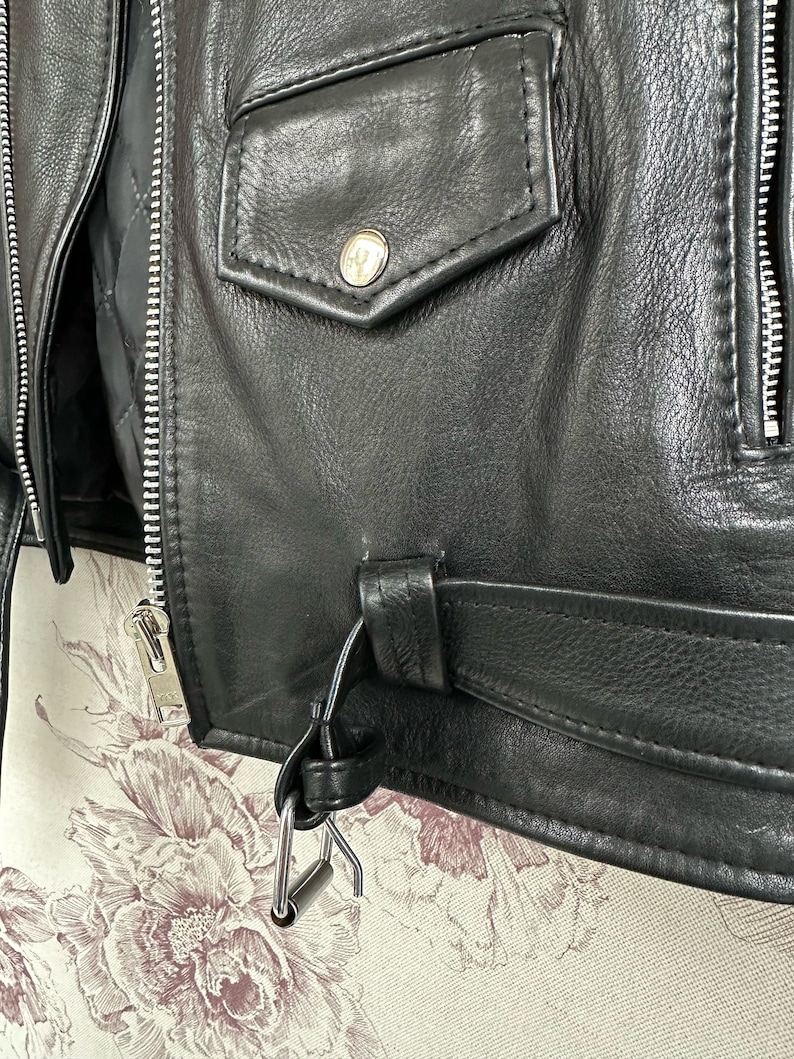 May include: Black leather jacket with a zipper closure, a large flap pocket on the front, and a belt with a metal buckle.