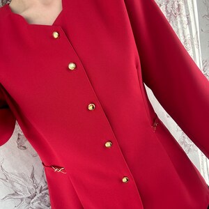 Puede incluir: Una chaqueta roja con botones dorados y cuello en V.