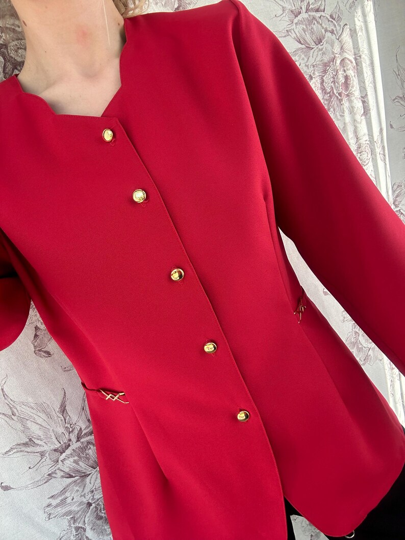 Puede incluir: Una chaqueta roja con botones dorados y cuello en V.