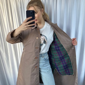 May include: A brown long-sleeved trench coat with a plaid lining. The coat has a button closure and a belt.