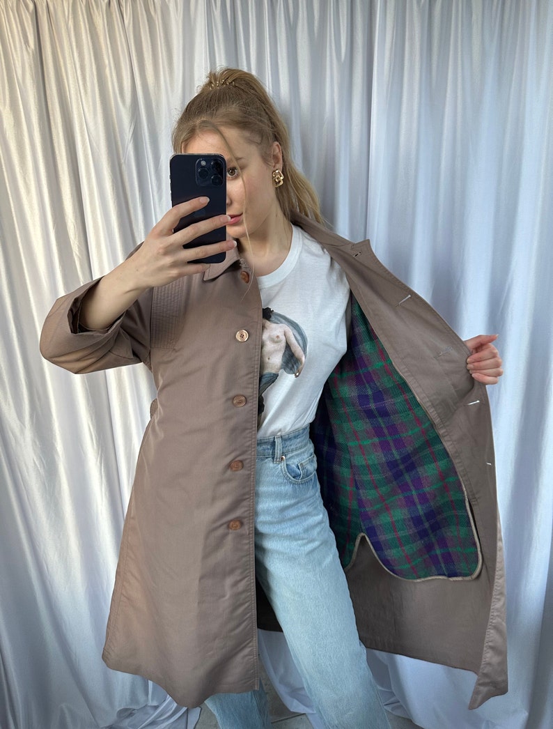 May include: A brown long-sleeved trench coat with a plaid lining. The coat has a button closure and a belt.