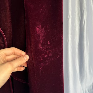 May include: Close-up of a burgundy velvet fabric with a slight sheen. The fabric has a few light-colored spots.