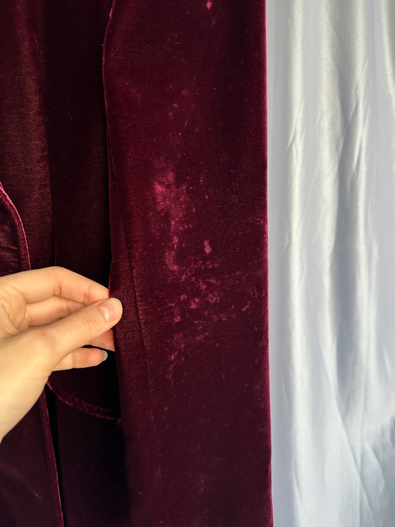May include: Close-up of a burgundy velvet fabric with a slight sheen. The fabric has a few light-colored spots.