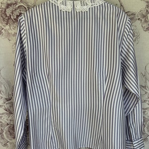 Pode incluir: Uma camisa de manga comprida listrada em branco e cinza com uma gola de renda branca.