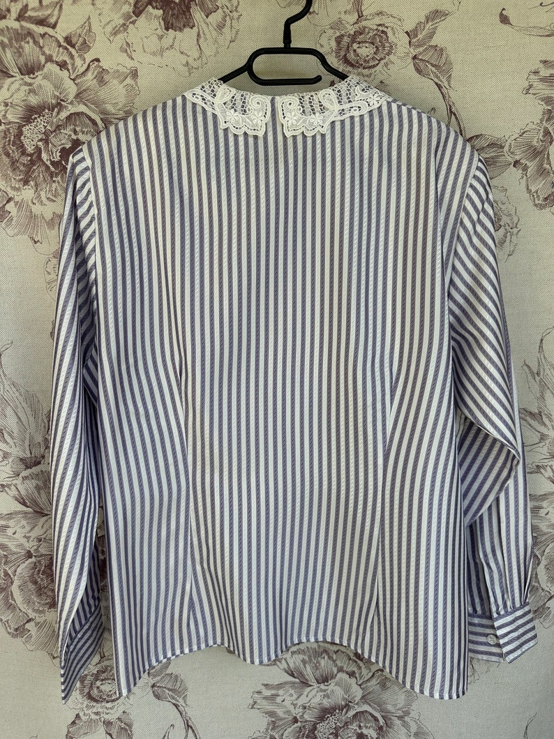 Pode incluir: Uma camisa de manga comprida listrada em branco e cinza com uma gola de renda branca.