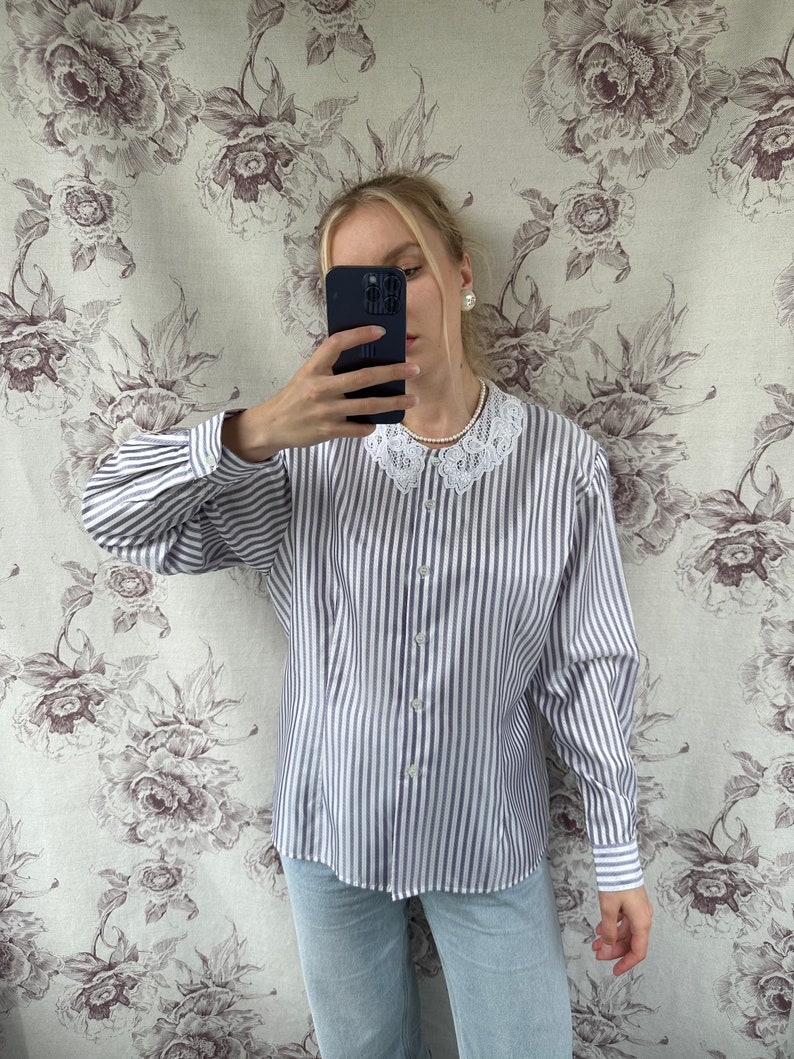 Pode incluir: Uma camisa de manga comprida listrada em branco e roxo com uma gola de renda branca. A camisa tem um fecho de bot&otilde;es na frente e mangas compridas com punhos de bot&otilde;es.