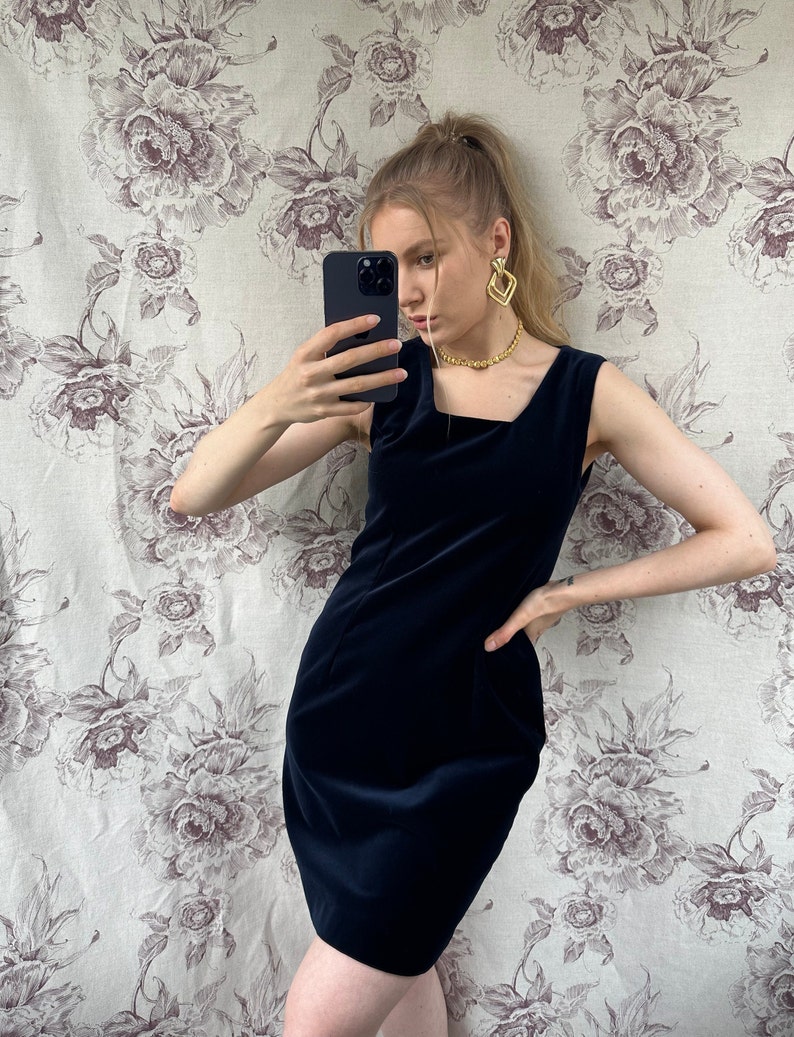 Pu&ograve; includere: Un abito in velluto blu navy senza maniche con scollo quadrato. L'abito &egrave; aderente e ha una lunghezza corta.