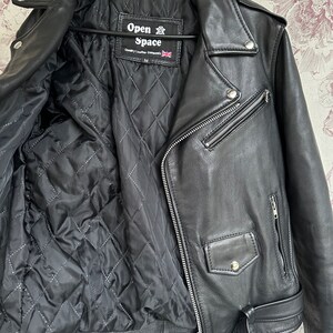 May include: Black leather motorcycle jacket with a quilted lining. The jacket has a zipper closure, two pockets, and a belt. The label on the jacket reads "Open Space" and "Quality Leather Garments".