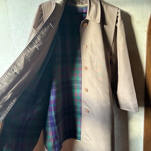 May include: A brown trench coat with a plaid lining. The coat has a button closure and a collar.