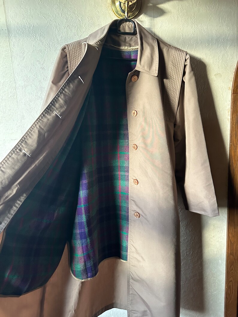 May include: A brown trench coat with a plaid lining. The coat has a button closure and a collar.