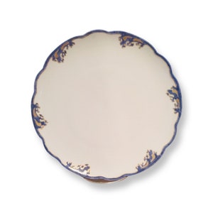 May include: A white ceramic cake stand with a scalloped edge and blue and gold floral design.
