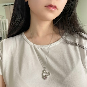 May include: A silver chain necklace with a Mickey Mouse-shaped pendant featuring a pink crystal. The pendant is hollow and has a delicate design.