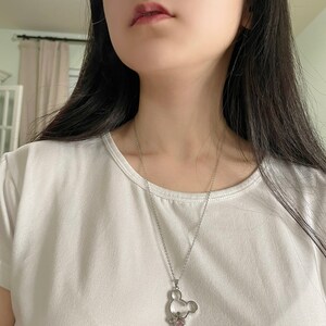 May include: A silver chain necklace with a silver Mickey Mouse pendant featuring a pink crystal.