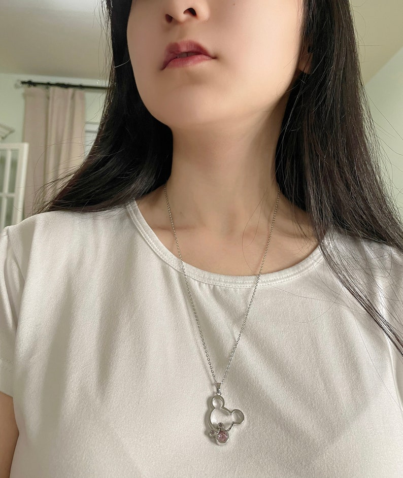May include: A silver chain necklace with a silver Mickey Mouse pendant featuring a pink crystal.