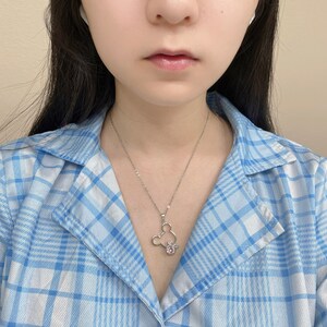 May include: A silver necklace with a Mickey Mouse pendant featuring pink rhinestones. The necklace is worn by a person wearing a blue and white plaid shirt.