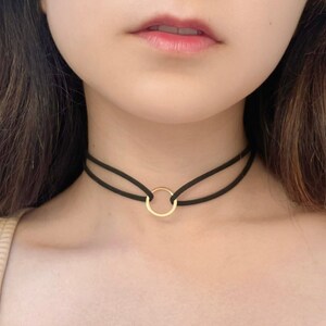 Puede incluir: Un collar gargantilla negro con un colgante circular dorado.