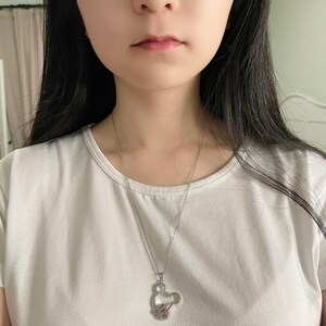 May include: A silver chain necklace with a Mickey Mouse pendant featuring a pink crystal. The pendant is a hollow outline of Mickey Mouse's head with a small pink crystal in the center.