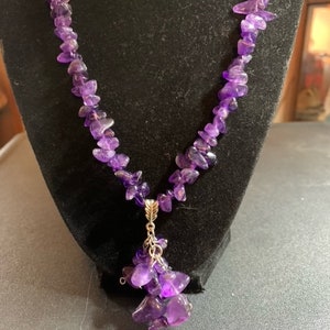 May include: A purple amethyst necklace with a pendant made of multiple amethyst stones. The pendant is attached to the necklace with a silver chain.