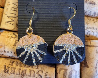 May include: A pair of cork earrings with a black and silver design. The earrings are round and have a gold hook.