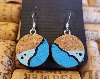 May include: A pair of cork earrings with a blue, white, and black abstract design. The earrings are on a black background.