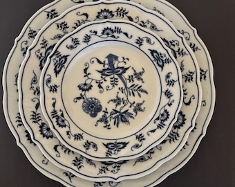 May include: Three white porcelain plates with a blue floral design. The plates are stacked, with a scalloped edge and a detailed pattern of flowers and leaves. The plates are a classic style.