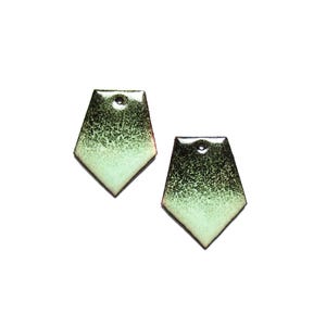 Puede incluir: Dos pendientes geométricos con un diseño moteado en negro y verde claro. Los pendientes tienen forma de escudo con un agujero en la parte superior para colgar. Los bordes están delineados en color marrón rojizo.
