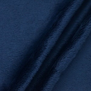 May include: Close-up of a navy blue plush fabric with a soft, textured surface. The fabric is folded, creating shadows and highlighting the depth of the material. The image showcases the rich color and tactile quality of the textile.