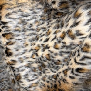 Puede incluir: Una tela de piel sintética con un denso estampado de leopardo. La textura consiste en fibras sintéticas suaves en tonos crema, bronceado y marrón, acentuadas con manchas de color gris oscuro y negro que crean un aspecto animal realista y detallado.