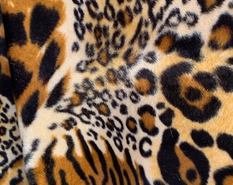 Könnte beinhalten: Nahaufnahme eines Kunstfellstoffs mit Leoparden- und Tigermuster. Der Stoff weist eine Mischung aus beigen, braunen und schwarzen Flecken und Streifen auf, wodurch ein strukturiertes und tierisches Design entsteht. Das Material wirkt weich und plüschig.
