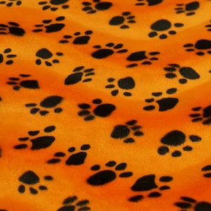 May include: Orange fabric with a black paw print pattern. The fabric has a fuzzy texture.