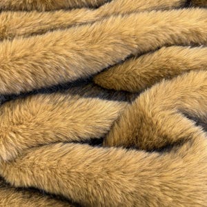 May include: A dense, long-pile faux fur fabric featuring a warm golden-brown color palette. The texture consists of soft, multi-tonal fibers with darker brown and black undertones visible at the base, creating a layered, realistic appearance.