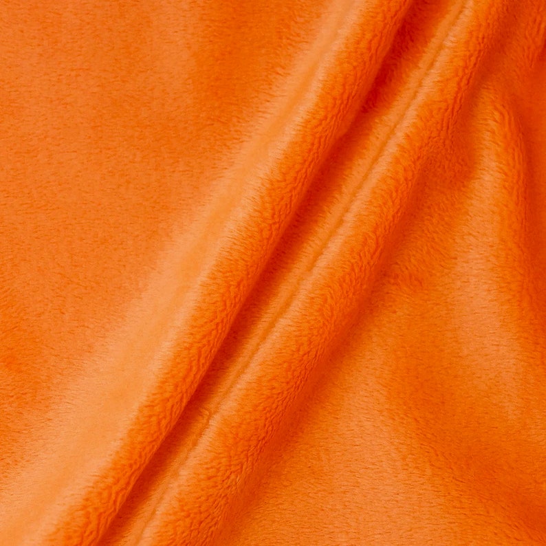 Puede incluir: Primer plano de una tela de color naranja brillante con una textura suave y peluda. La tela est&aacute; doblada por la mitad, creando una l&iacute;nea diagonal a trav&eacute;s de la imagen.