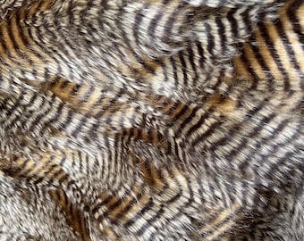 Könnte beinhalten: Nahaufnahme eines braunen und schwarzen Kunstpelzes mit einem gestreiften Muster. Der Stoff hat eine weiche, plüschige Textur.