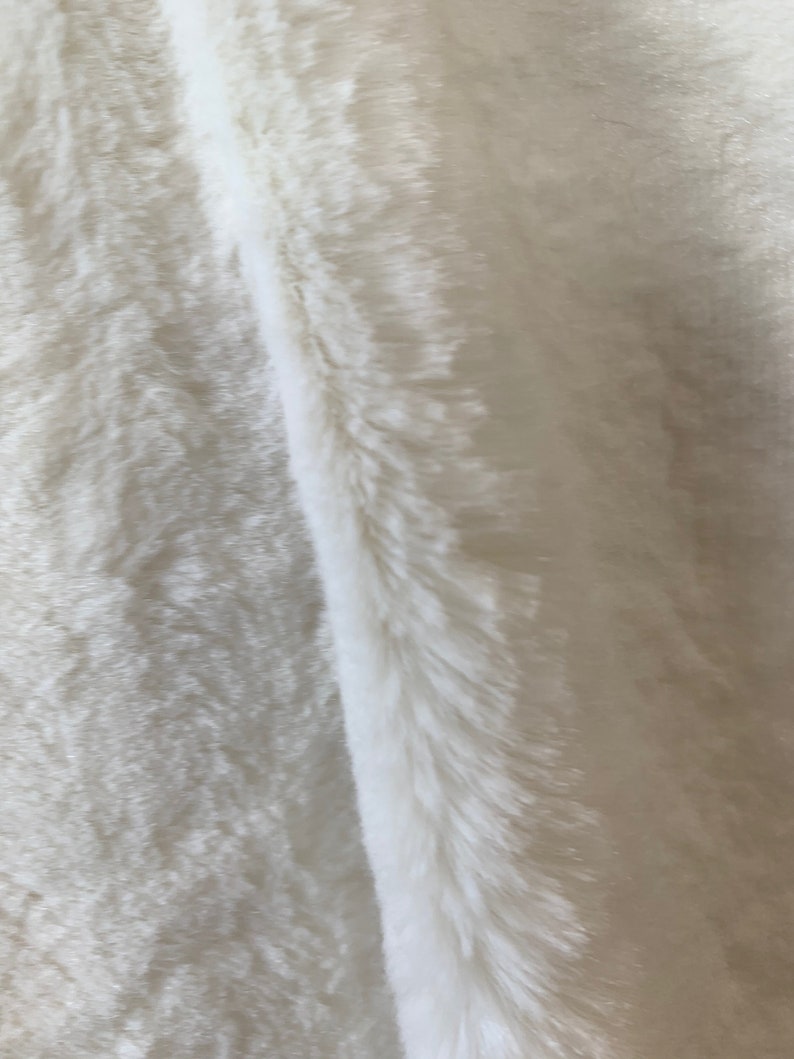 May include: A close-up of a white faux fur fabric. The fabric has a soft, fluffy texture and a subtle sheen.