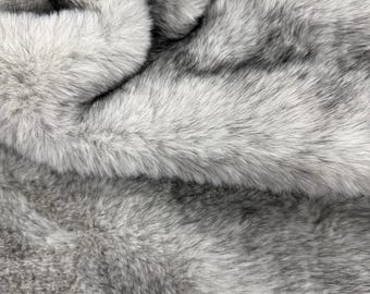 Könnte beinhalten: Ein dicker, plüschiger Kunstfellstoff mit dichtem Flor in einer variierenden Farbpalette aus Silber, Anthrazit und Weiß. Das Material weist eine weiche, zottelige Textur mit langen, feinen Fasern auf, die tiefe Falten und Schatten bilden.