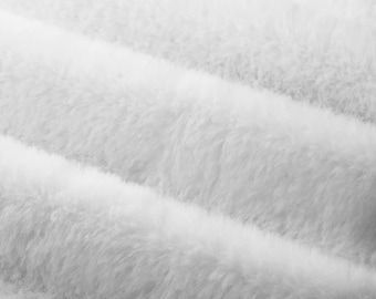 Könnte beinhalten: Weißer, flauschiger Stoff mit weicher, plüschiger Textur. Der Stoff ist in der Mitte gefaltet und bildet eine glatte, gleichmäßige Oberfläche.