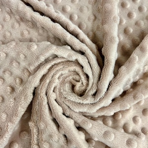May include: A close-up of a beige plush fabric with a textured pattern of small raised circles. The fabric is soft and fluffy, and it is perfect for making blankets, pillows, or other home decor items.