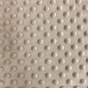 May include: Beige minky fabric with a textured pattern of small raised circles. The fabric is soft and plush, making it ideal for blankets, baby clothes, and other crafts.