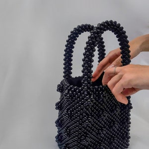 May include: A black beaded tote bag with two handles. The bag is made of small, round beads that are woven together in a pattern.