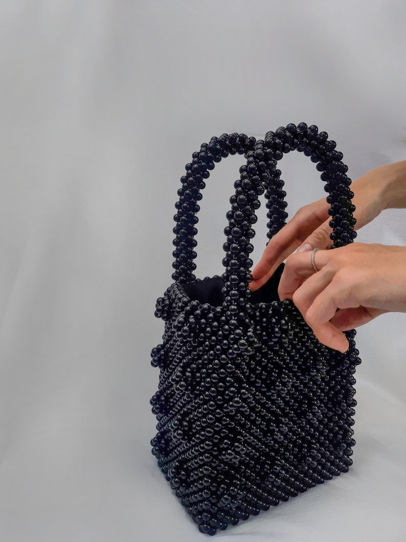 May include: A black beaded tote bag with two handles. The bag is made of small, round beads that are woven together in a pattern.