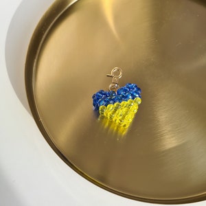 以下が含まれることがあります： 金色のトレイの上にある、青と黄色のビーズでできたハート型のキーホルダー
